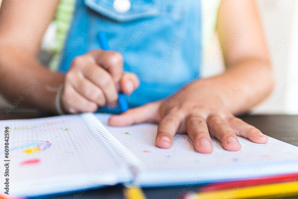 Girl drawing hand on notebook with crayon